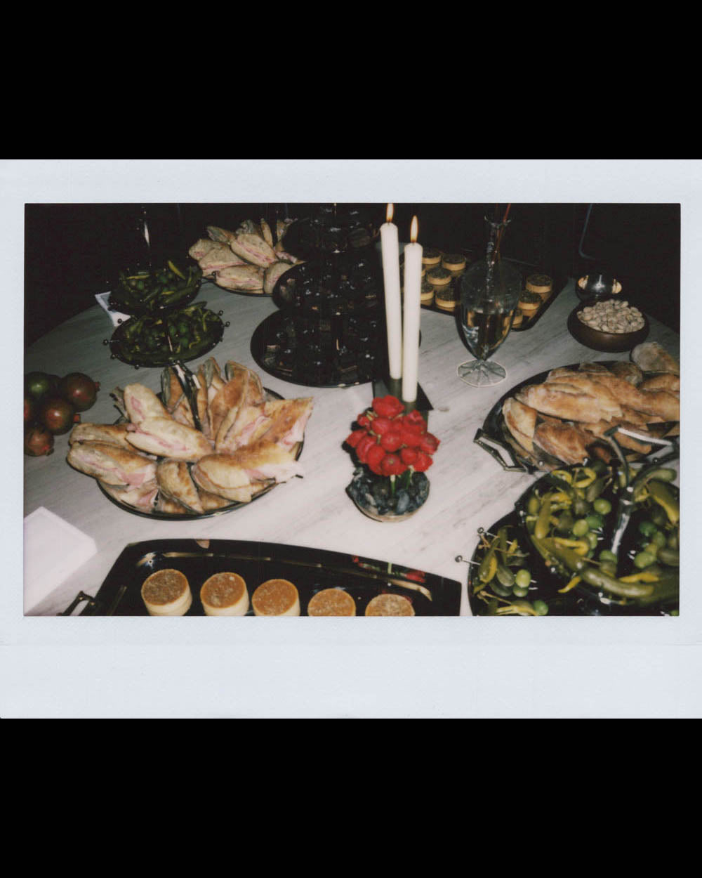 Table with assorted breads, sandwiches, olives, nuts, and lit candles in a dimly lit setting.