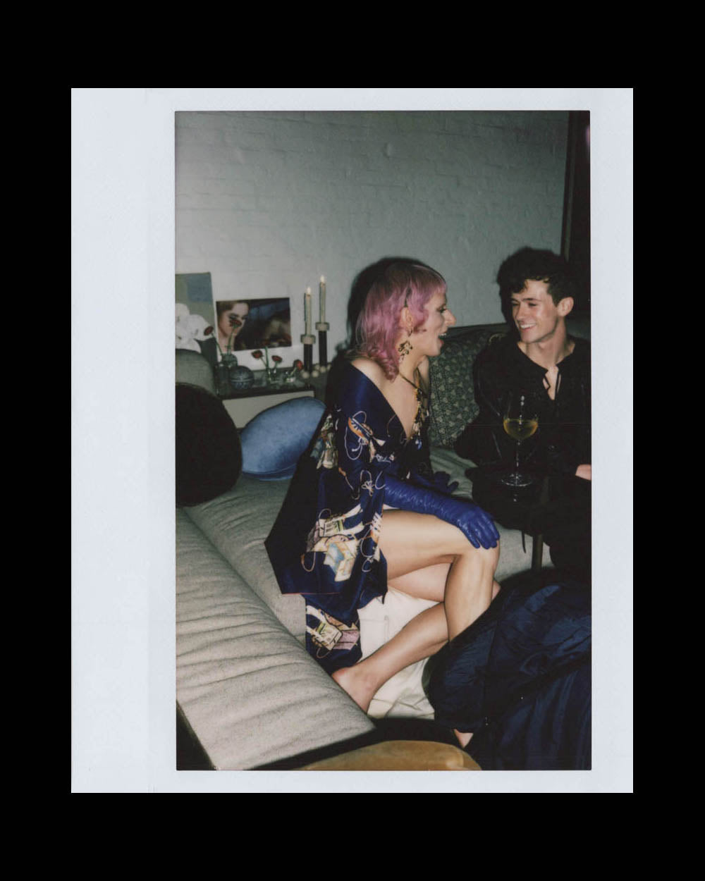 Two young people sitting closely on a couch indoors, smiling and engaging in conversation with drinks nearby.