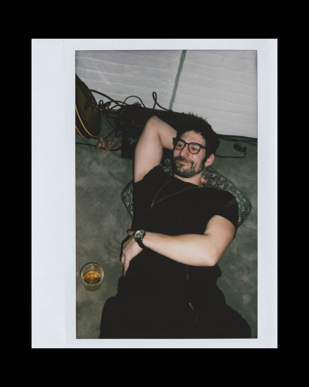 A man with glasses relaxing on a couch with one arm behind his head and a drink nearby.