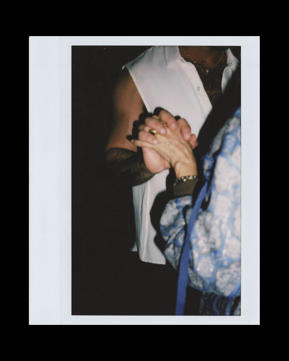 Close-up of two people holding hands, one wearing a sleeveless white shirt and the other in patterned blue clothing.