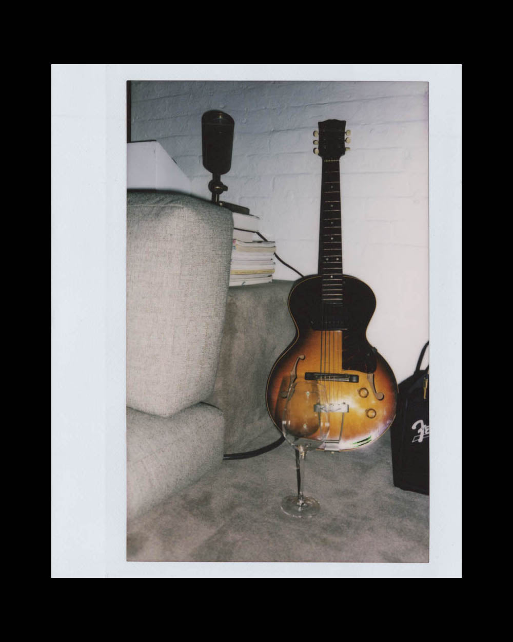 Vintage electric guitar resting on a carpet next to a glass of wine, couch, books, and a microphone stand nearby