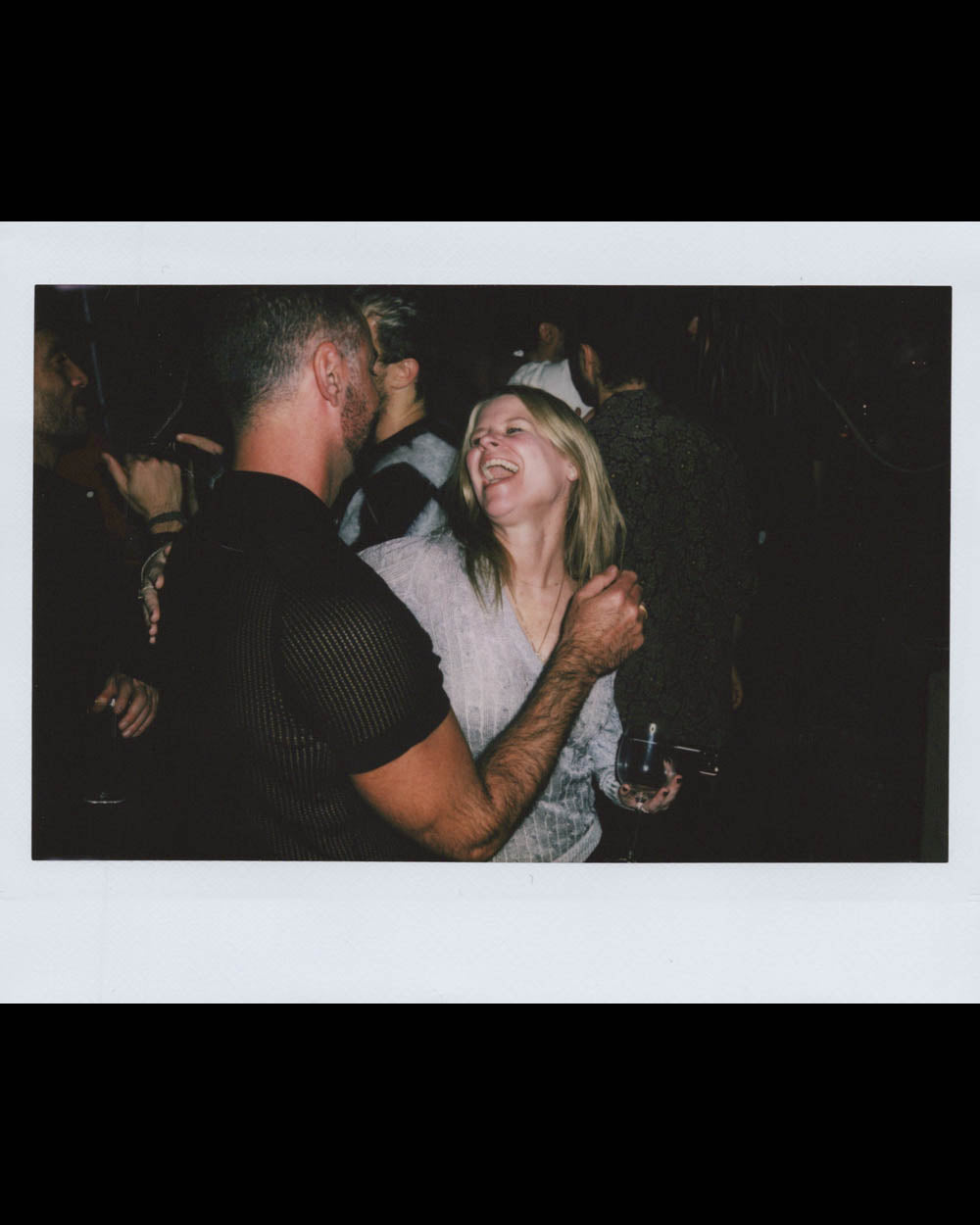 A man and woman smiling and dancing closely together in a dimly lit crowded indoor event.