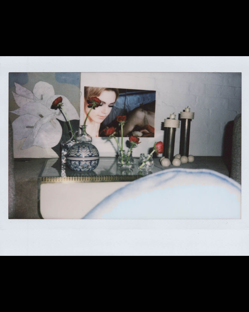 Tabletop with decorative vases holding red roses, a framed portrait, large flower artwork, and tall textured candle holders