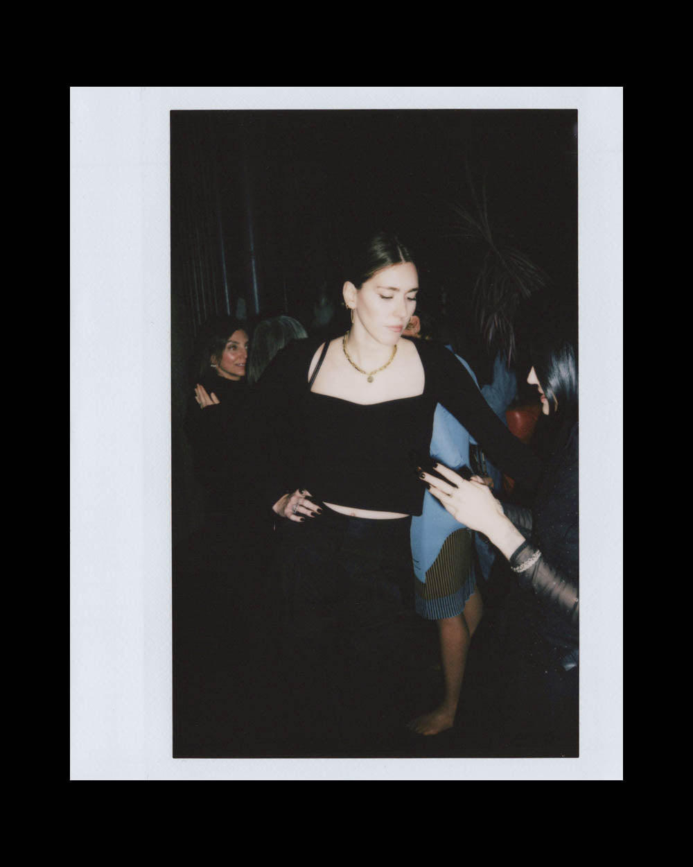 Woman in black top and skirt dancing or moving with another person in a dimly lit indoor setting