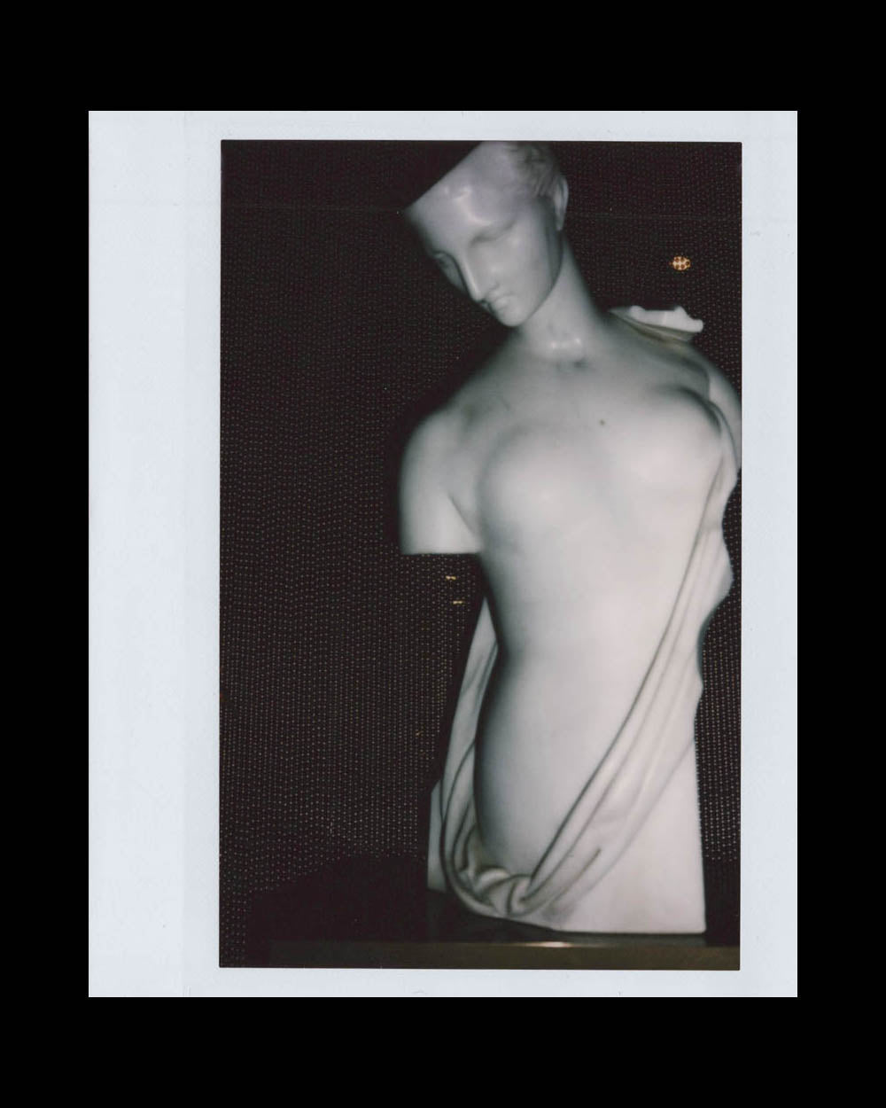Marble sculpture of a partially draped female torso with a tilted head against a dark backdrop