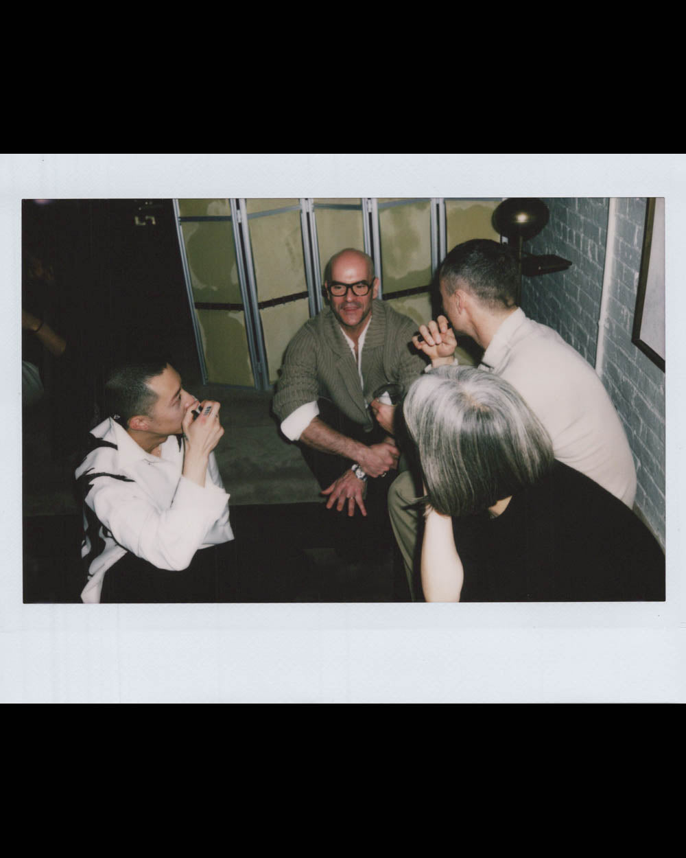 Four people sitting and conversing closely in a casual indoor space with exposed brick walls and muted lighting