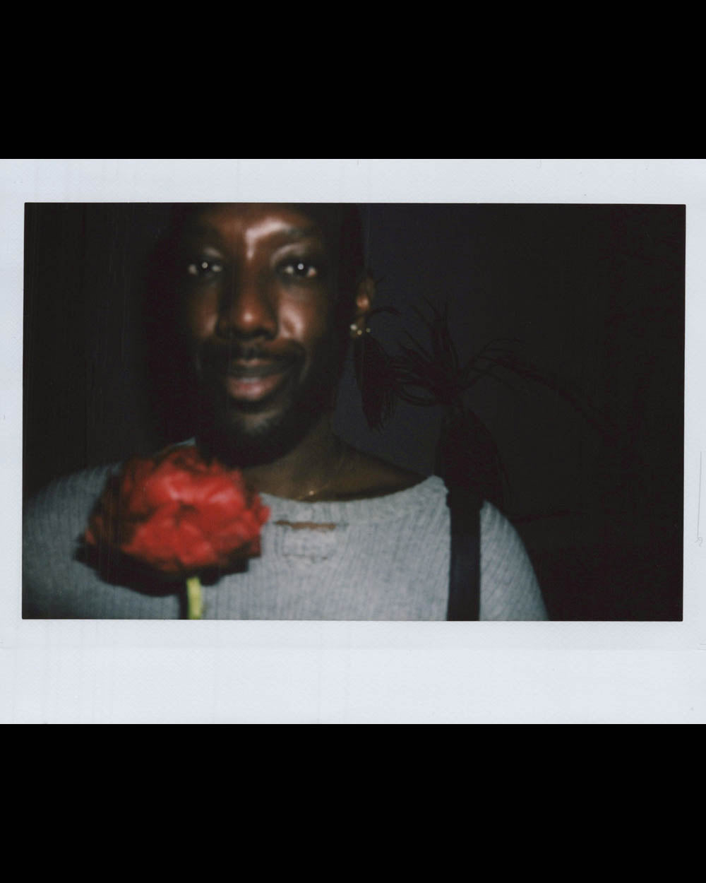 Person wearing light gray top holding a red flower close to the camera in a dimly lit setting