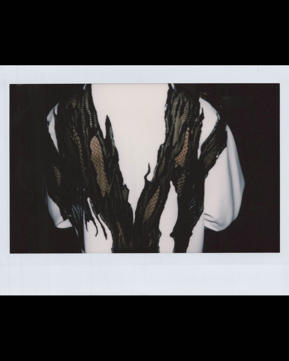 Back view of a person wearing a white garment with torn black lace fabric creating a V-shaped pattern.