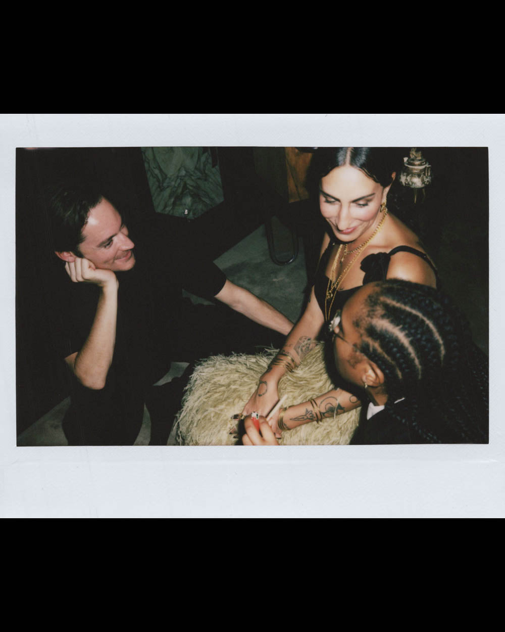 Three people seated closely, engaged in a conversation in a dimly lit setting with relaxed body language.