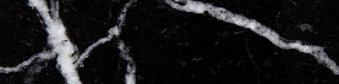 Close-up of black marble surface with irregular white veining and glossy texture against a dark background