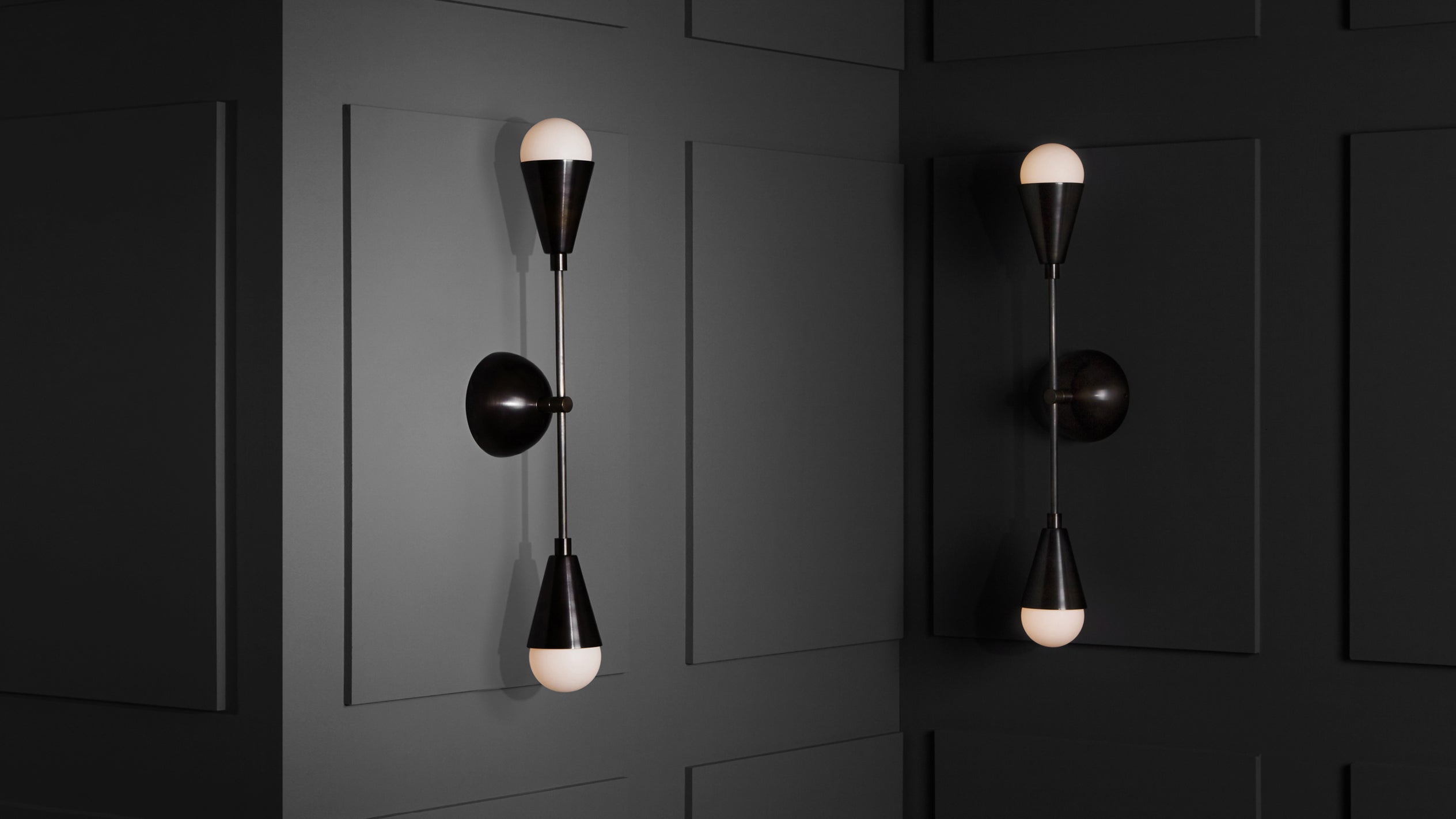 Two modern black wall sconces with white globe bulbs mounted on dark paneled wall panels