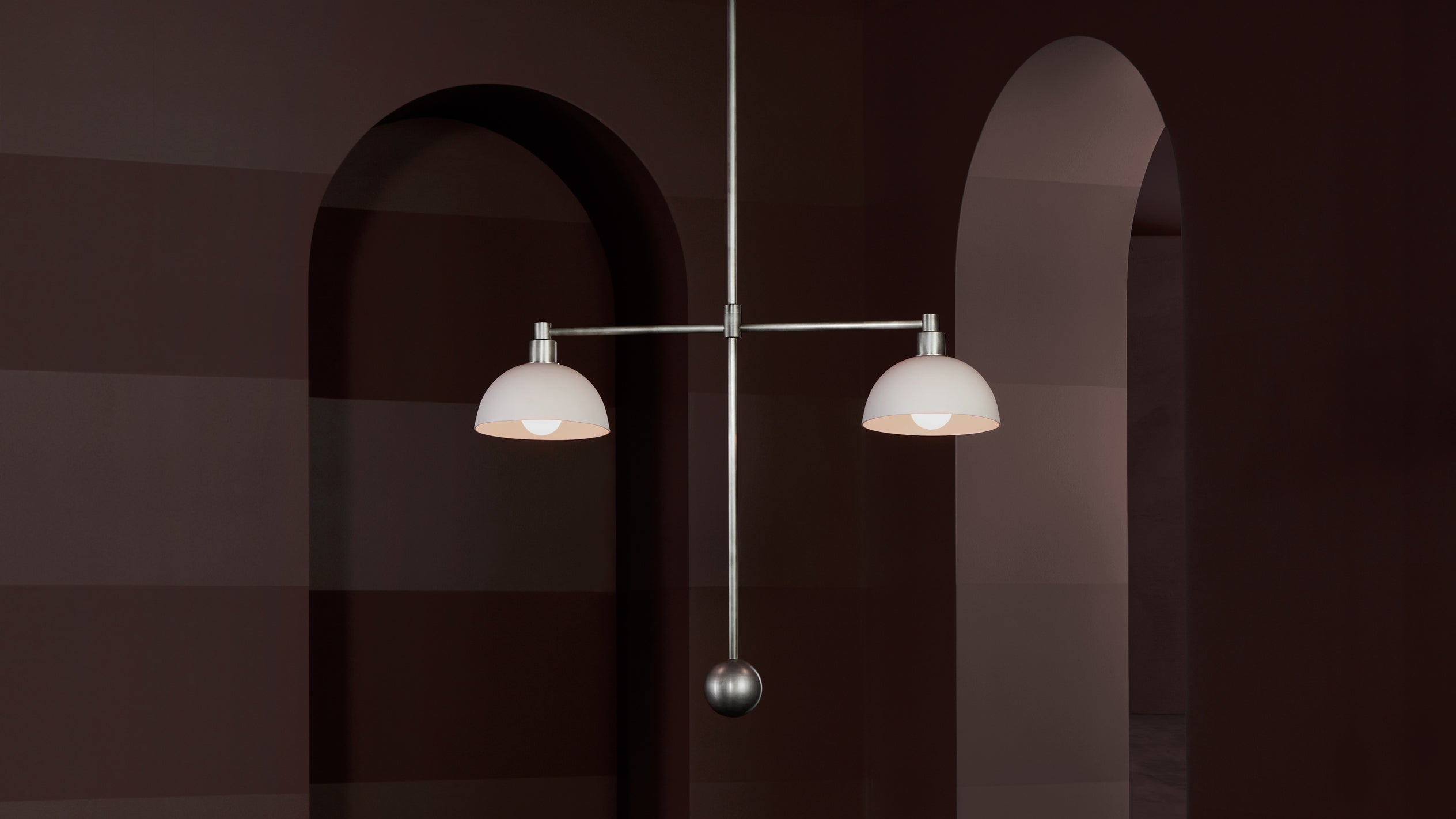 Minimalist silver double pendant light with white dome shades hanging in front of dark brown arched walls
