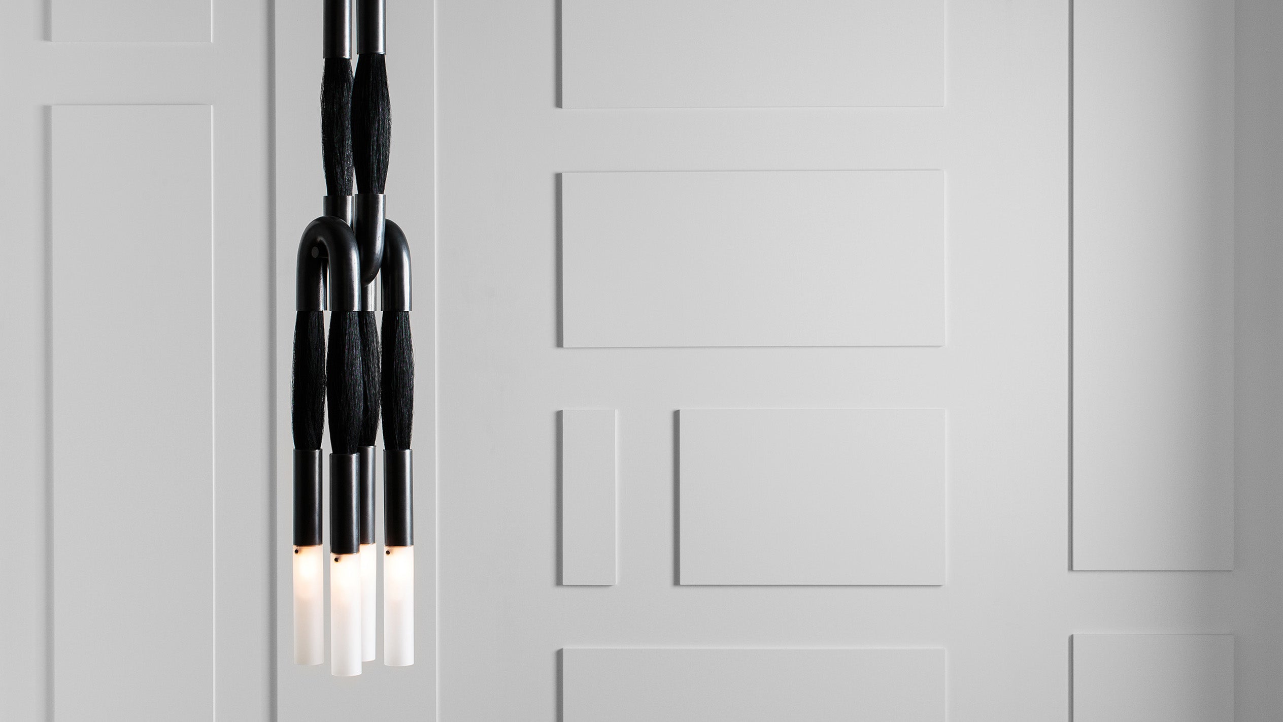 Close-up of minimalist black pendant lights with cylindrical bulbs hanging against a gray paneled wall background