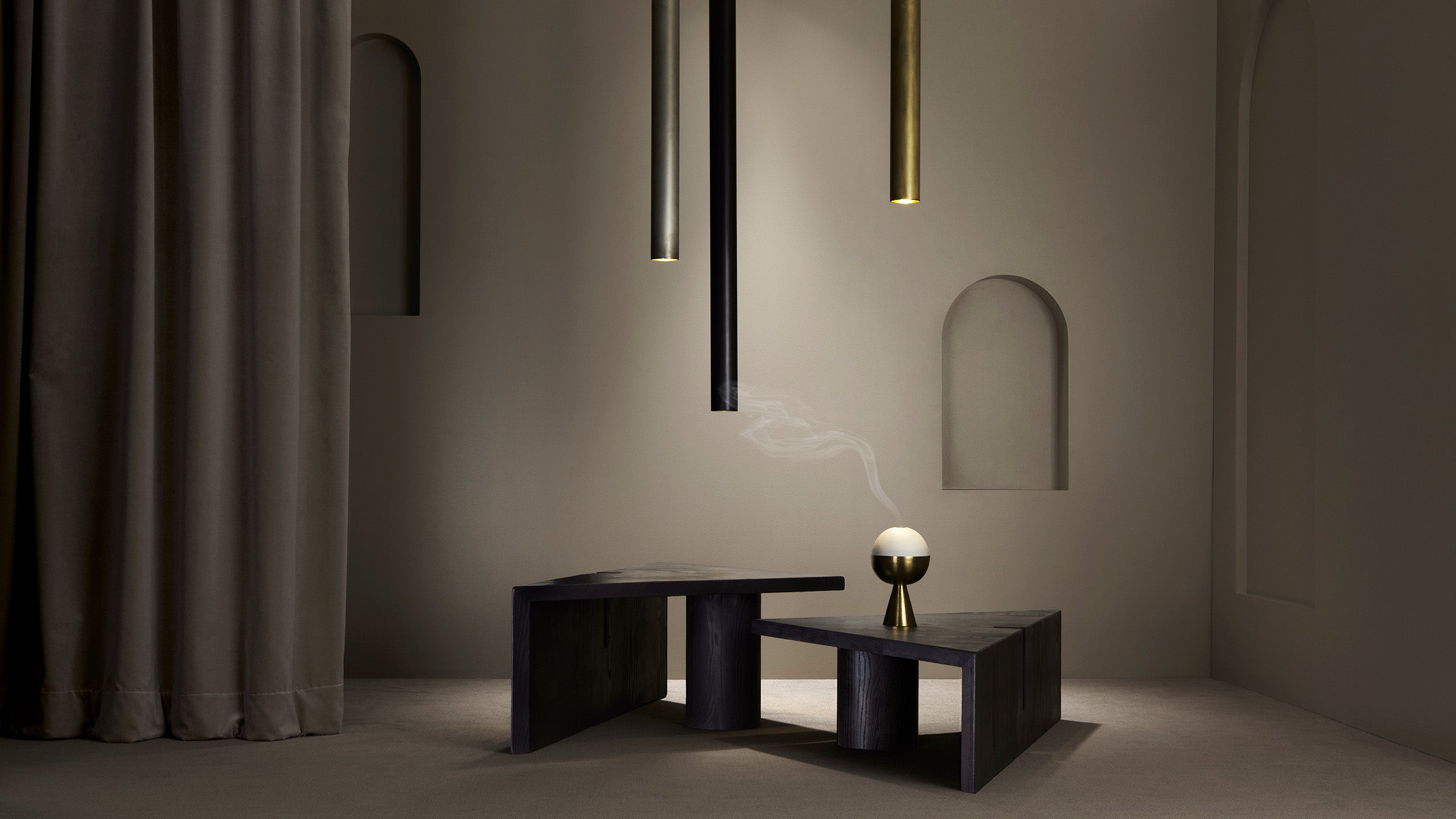 Minimalist interior with dark geometric coffee tables, suspended pendant lights, and a small incense burner emitting smoke