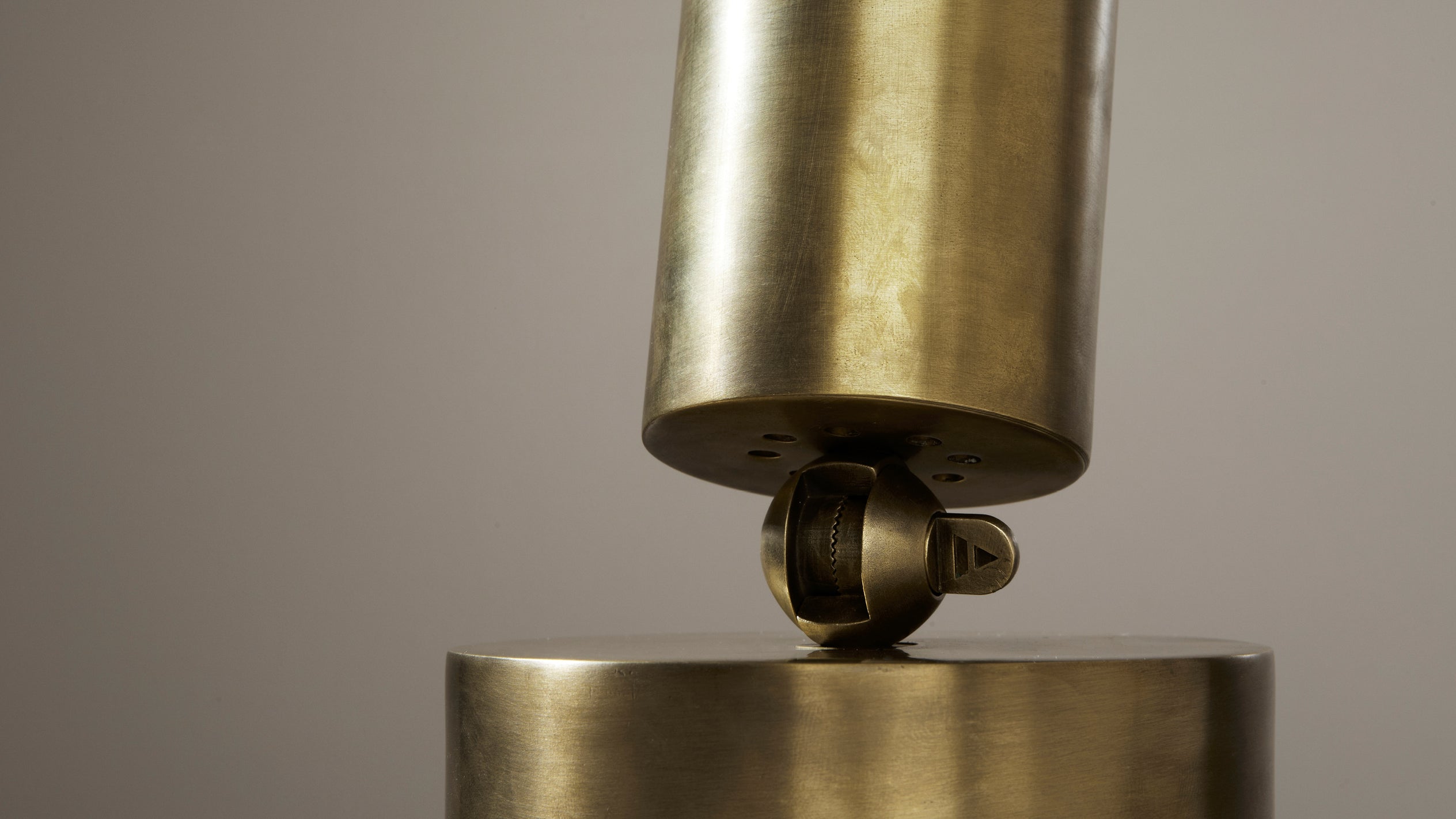 Close-up of a brass caster wheel connecting two cylindrical metallic components against a plain neutral background