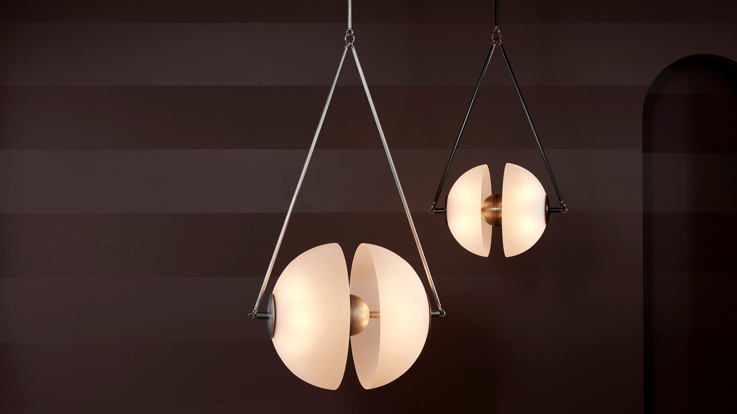 Two modern pendant lights with white curved shades suspended against a dark striped wall background