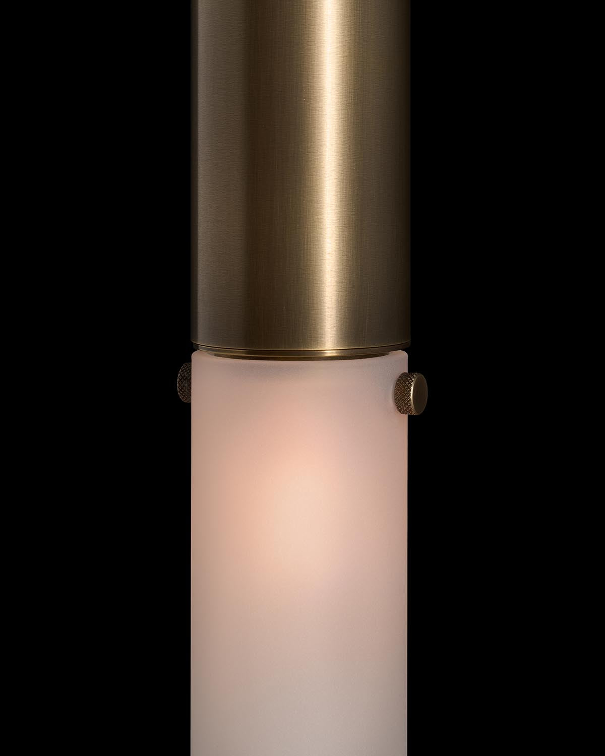 Close-up of a cylindrical pendant light with brushed brass finish and frosted glass diffuser on a black background