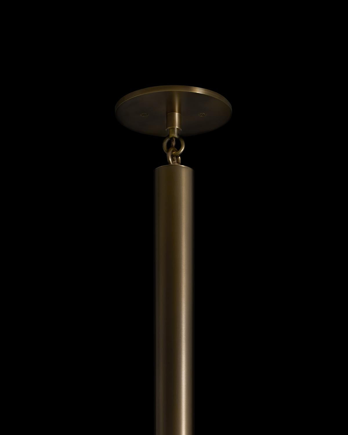 Close-up of a cylindrical brass pendant light fixture with round ceiling mount against a black background