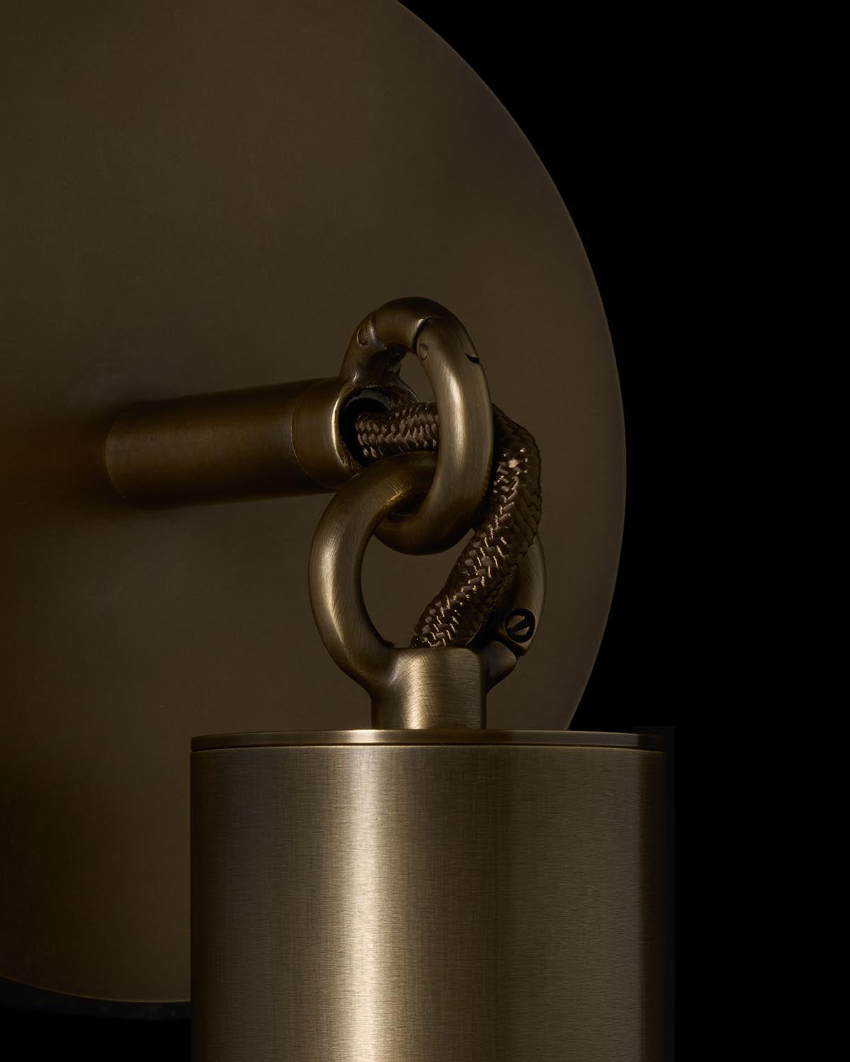 Close-up of brass wall sconce with detailed braided cord and circular backplate against a black background