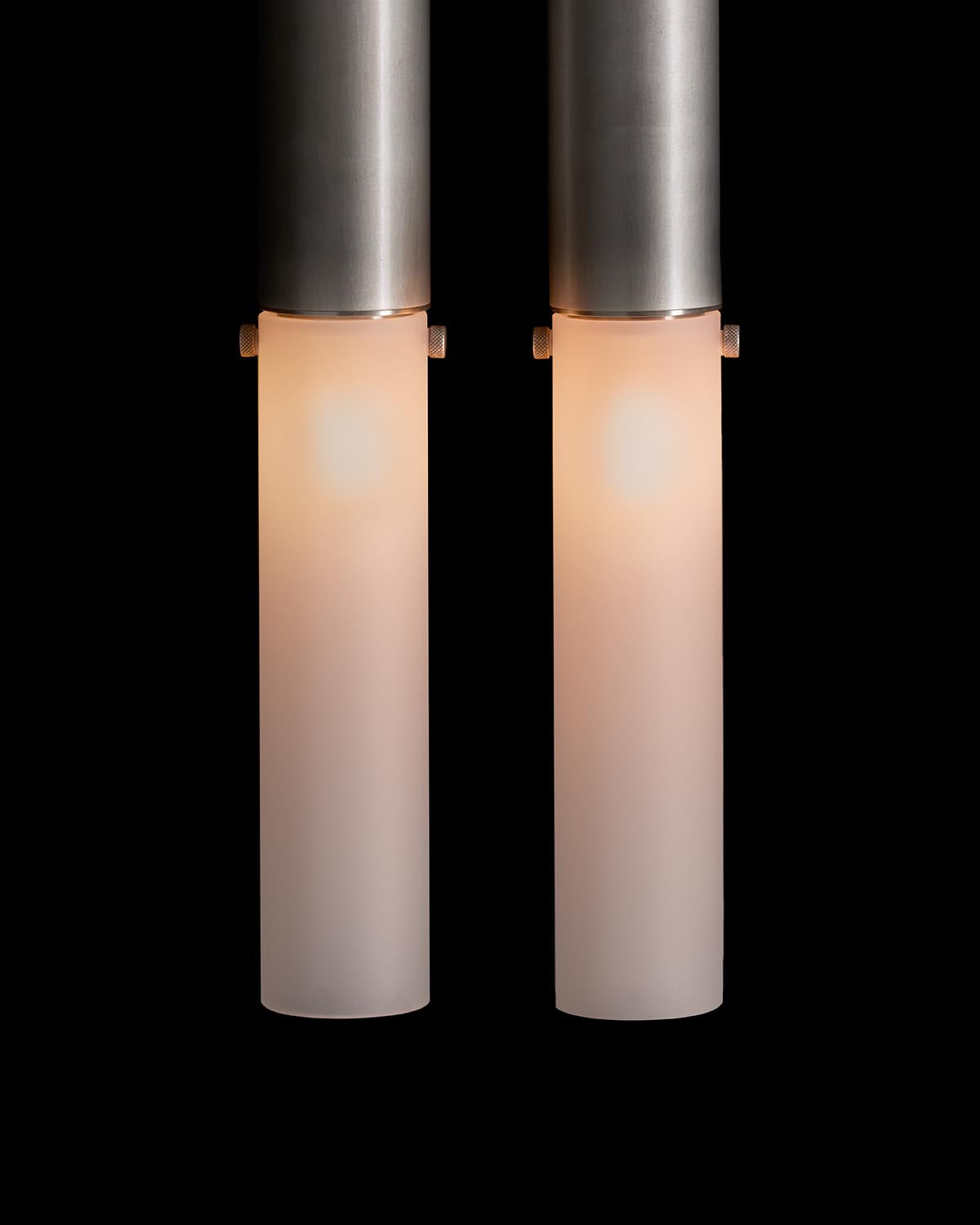 Pair of cylindrical wall sconces with frosted glass shades and brushed metal tops against a black background