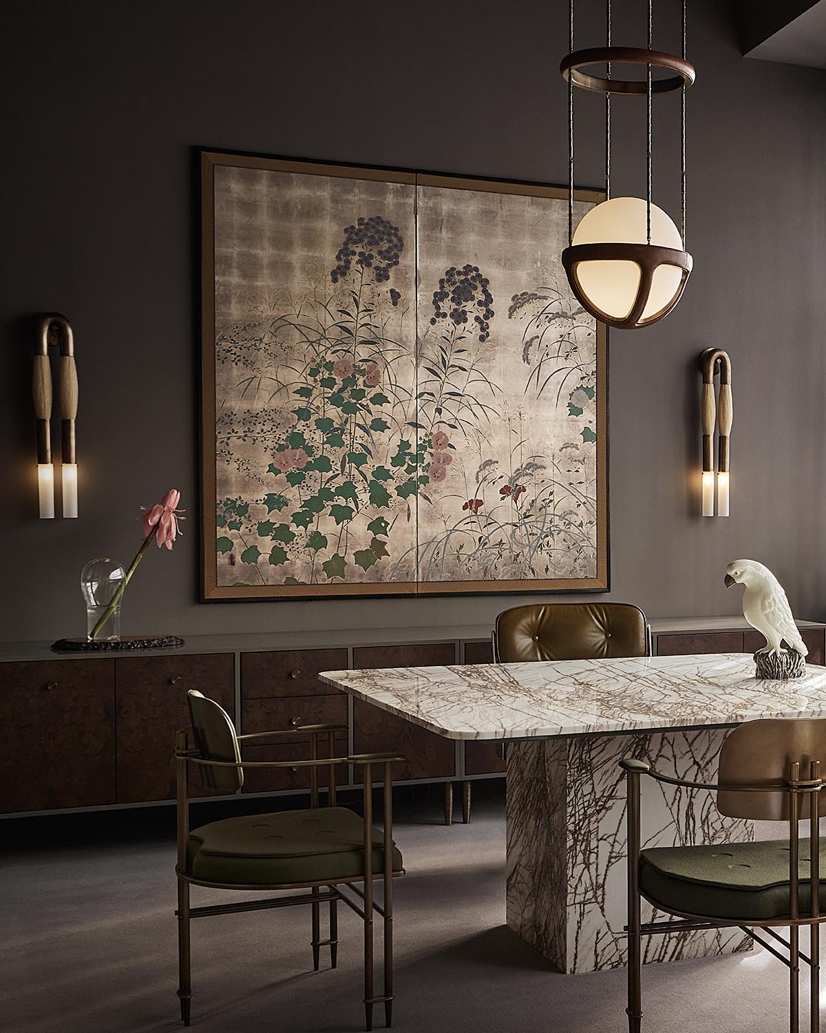 Modern dining room with a marble table, olive green chairs, wall-mounted horsehair sconces, and floral artwork on gray walls