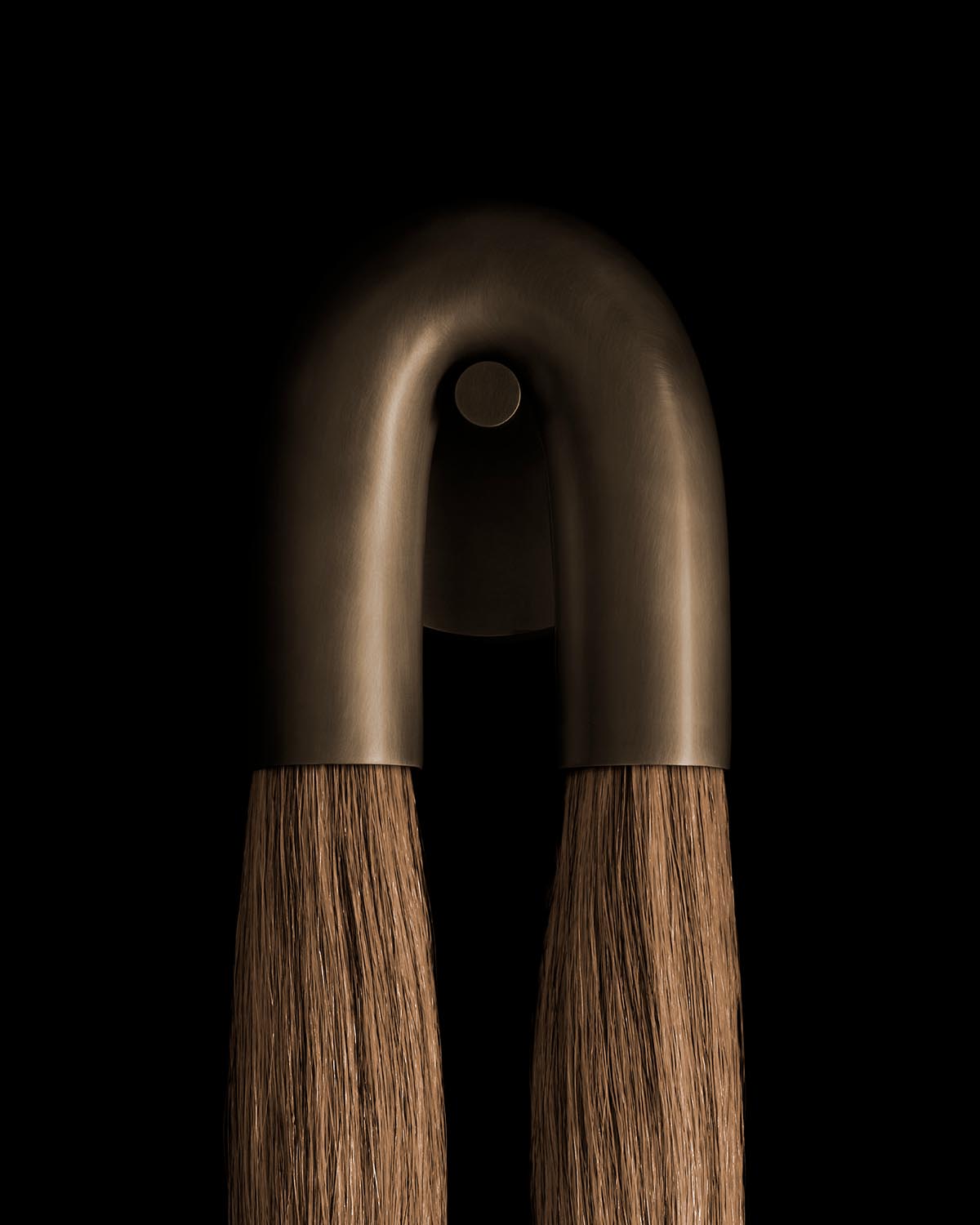 Close-up of a matte bronze curved sconce with natural horsehair strands hanging against a black background