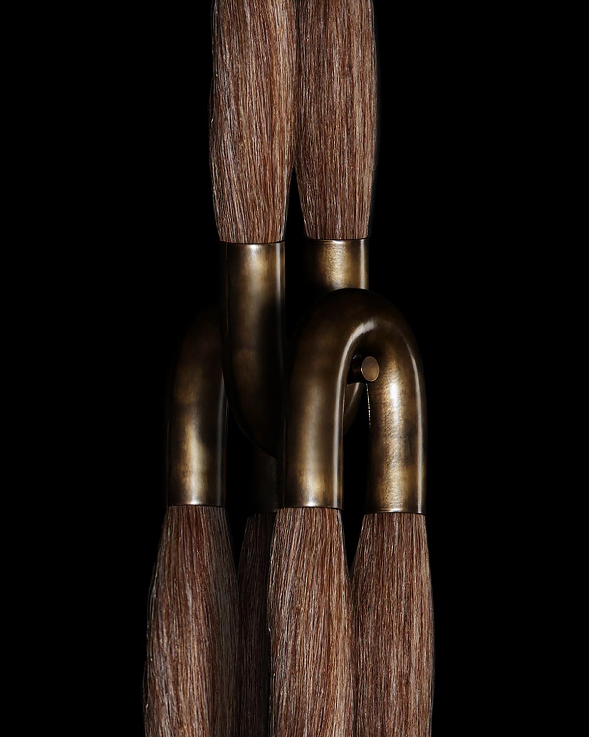 Close-up of intertwined bronze U-shaped tubes with brown horsehair tassels against a black background