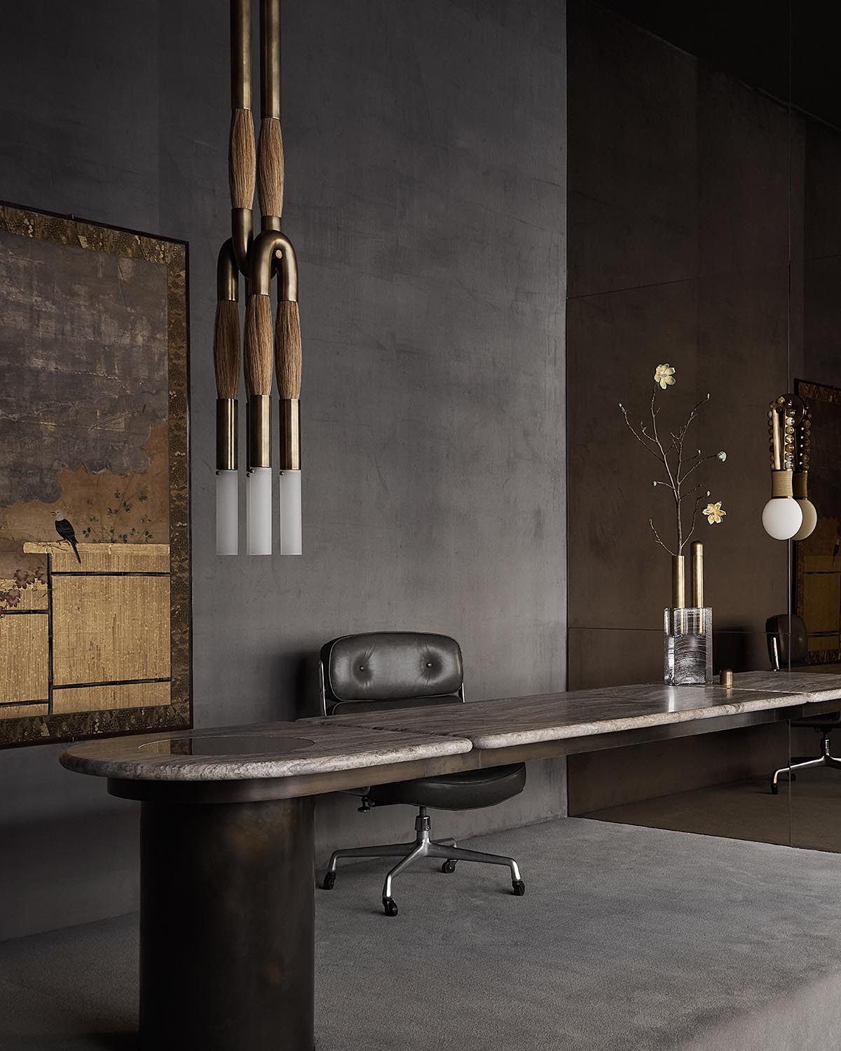 Minimalist workspace with a long marble table, black leather chair, decorative vase, and four pendant lights with wooden accents
