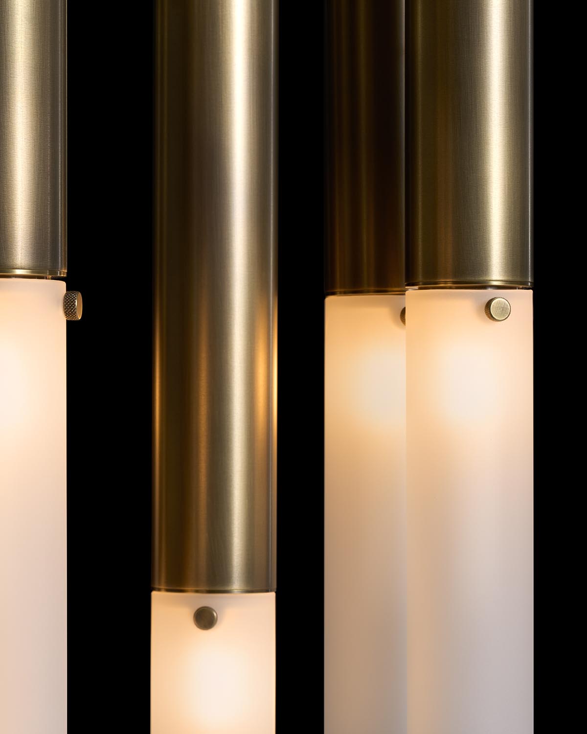 Close-up of brass cylindrical pendant lights with frosted glass shades on a black background