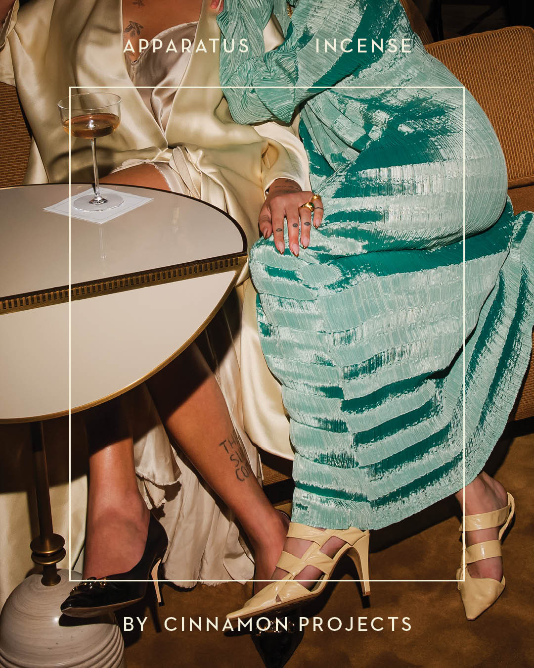 Two people seated at a round white table wearing satin and textured dresses with high-heeled shoes visible