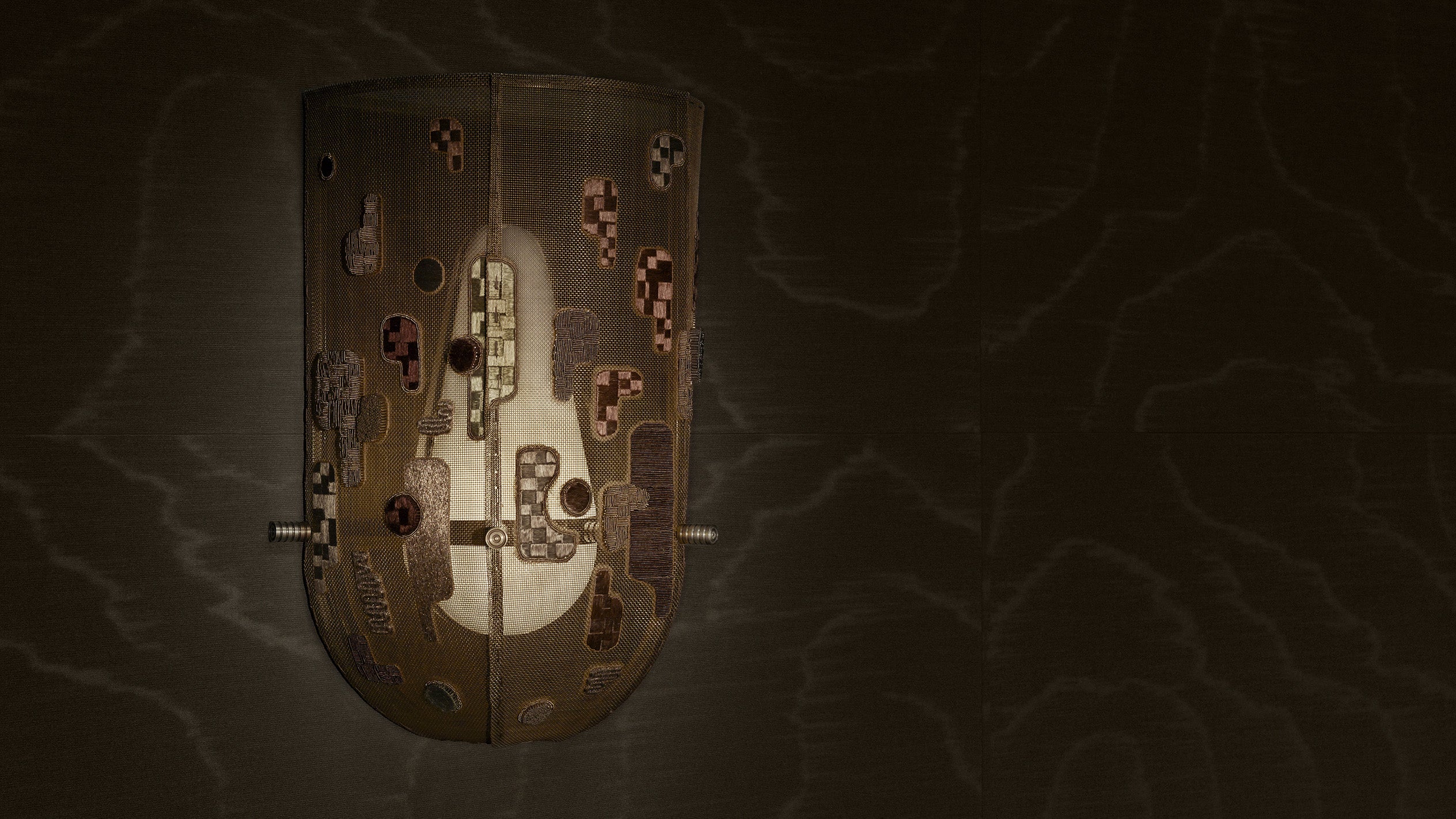 Dimly lit artistic wooden wall sconce with abstract cutouts and a softly glowing light inside on a dark textured background