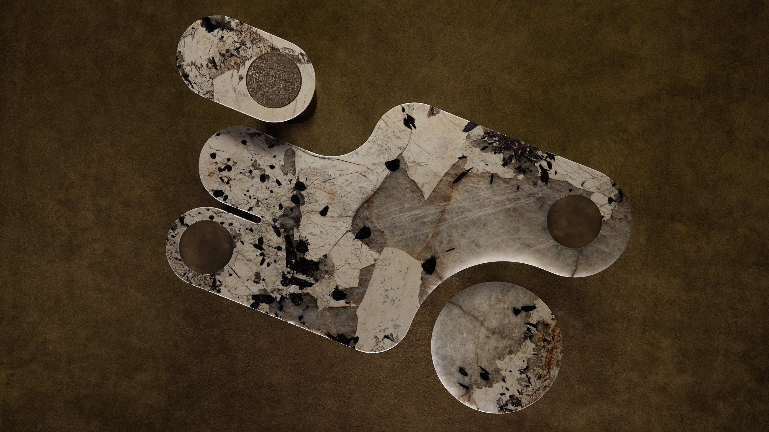 Abstract stone sculpture composed of interconnected rounded shapes with speckled black and beige textures on a brown surface