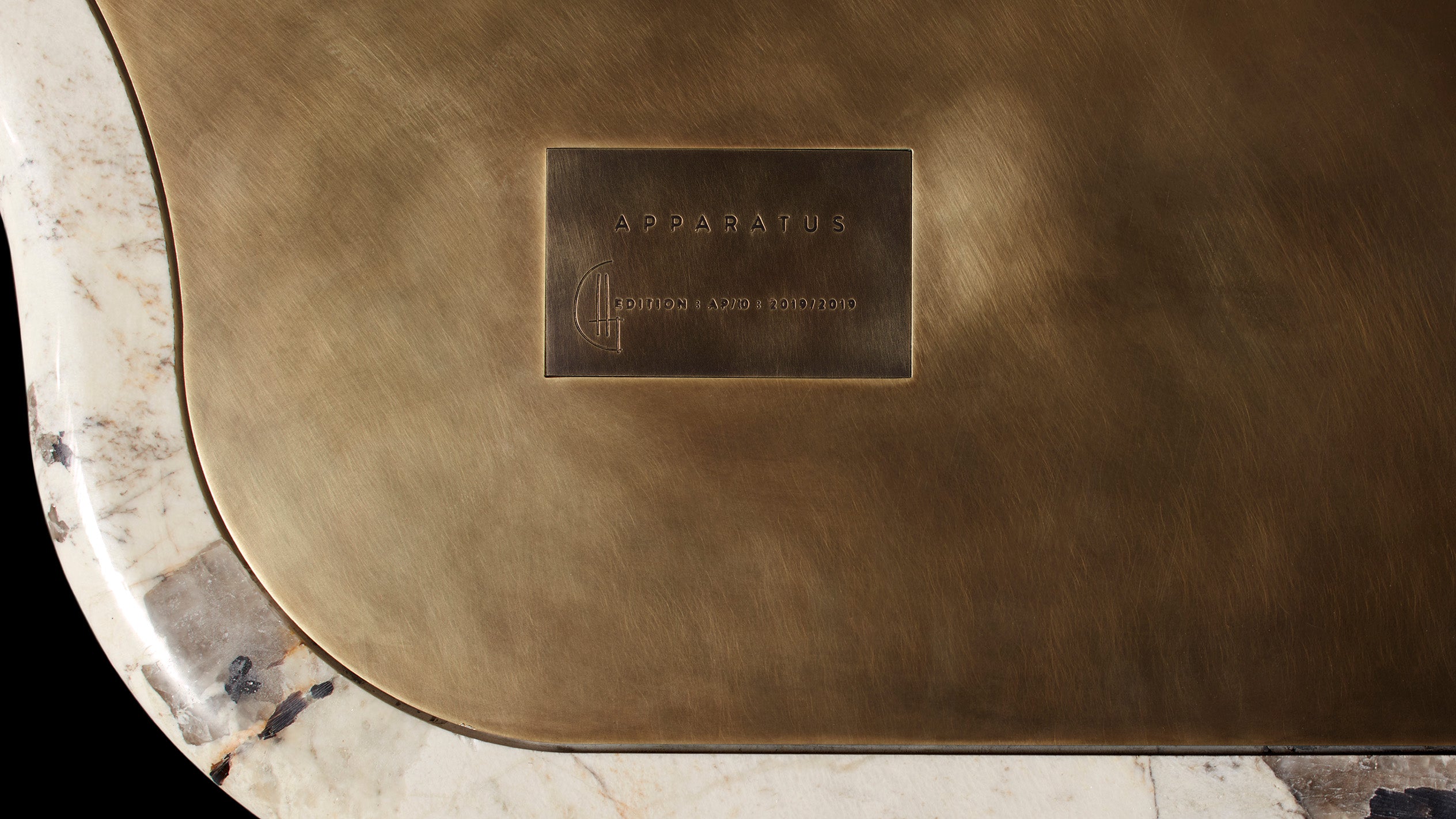Close-up of a brass plate embossed with text on a rounded beige marble surface against a black background