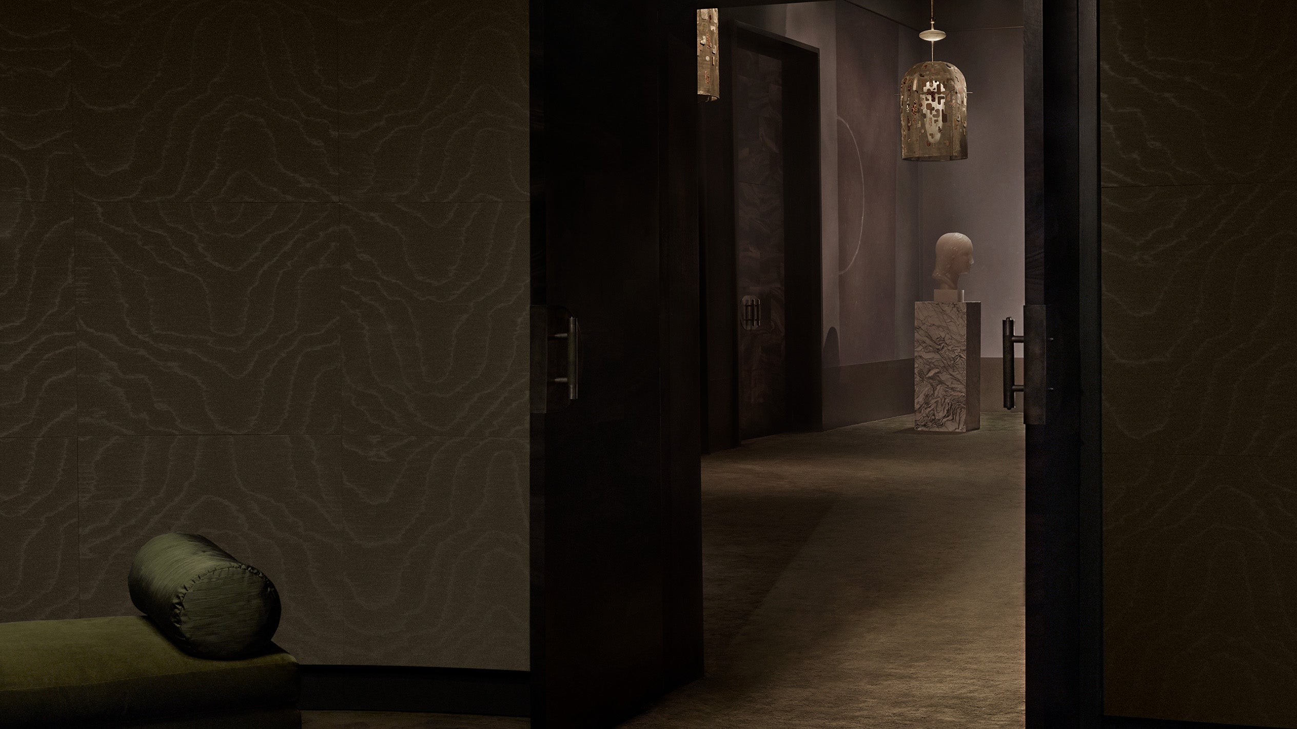 Dimly lit interior hallway with textured walls, an open door, a stone pedestal bust, and a hanging lantern light fixture.