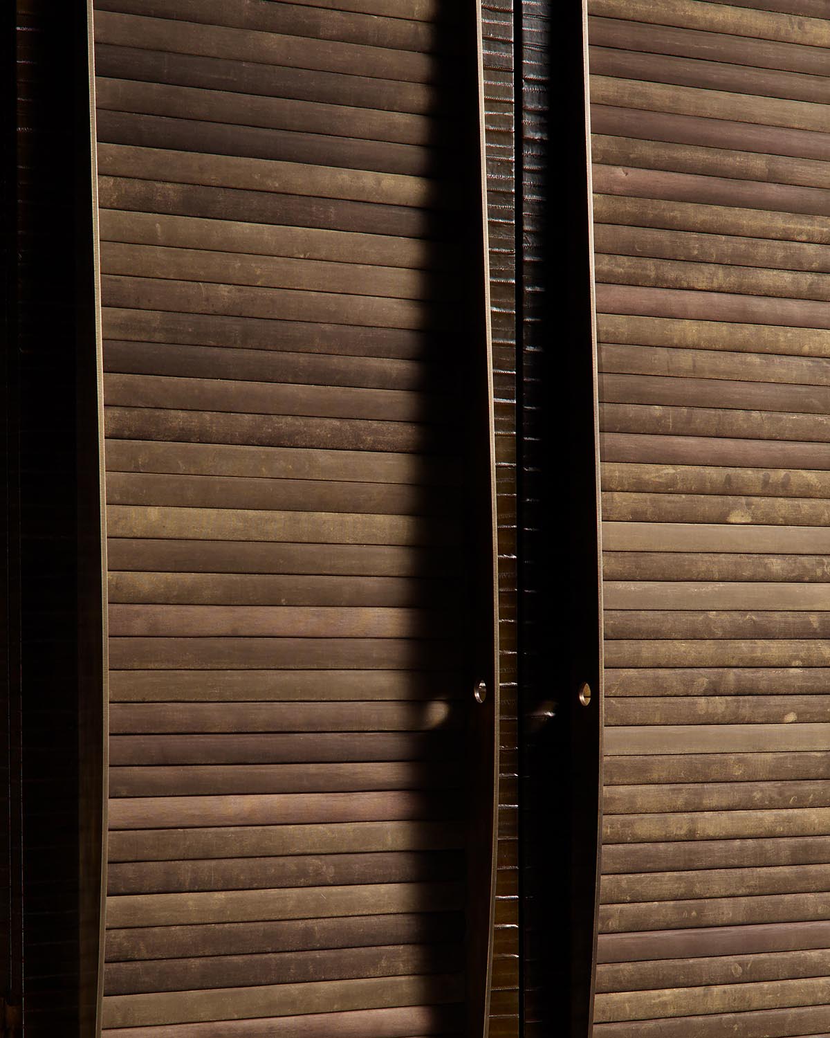 Close-up of a dark wooden cabinet with horizontal slats and rounded metal knobs in low lighting against a dark background