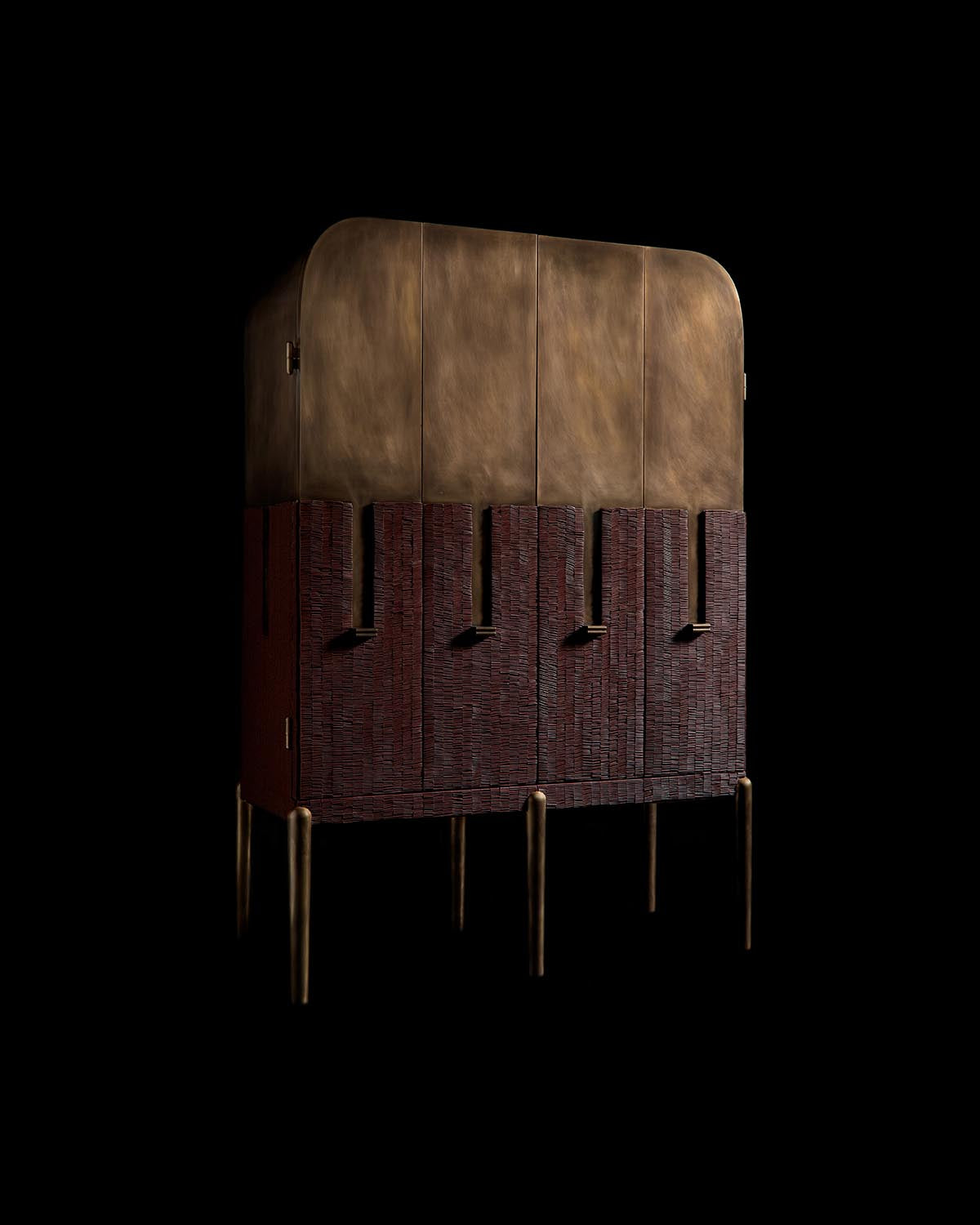 Tall cabinet with bronze upper panels and textured dark wood lower section, supported by slender bronze legs against black background