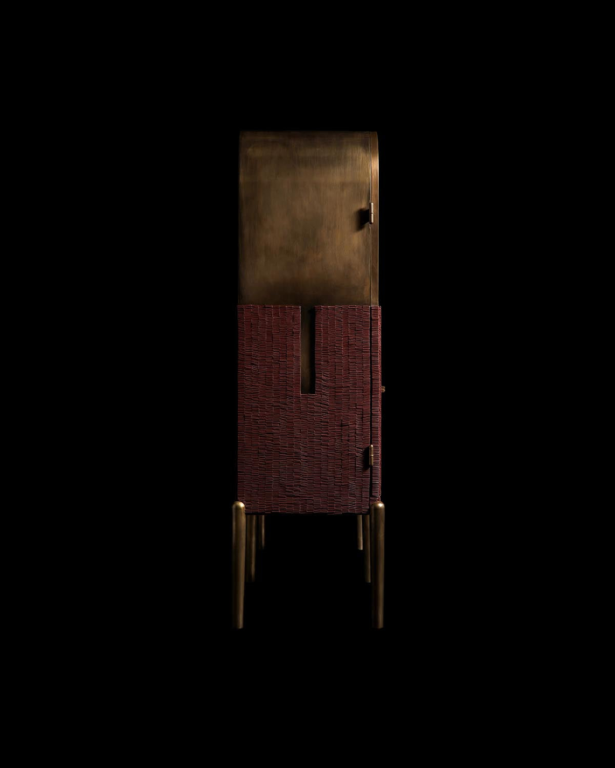 Tall cabinet with textured deep red lower doors and smooth dark bronze upper section on slender bronze legs against black background
