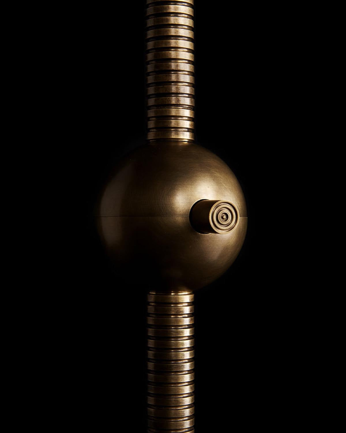 Close-up of metallic spherical joint connecting ribbed cylindrical segments with a small circular detail on a black background