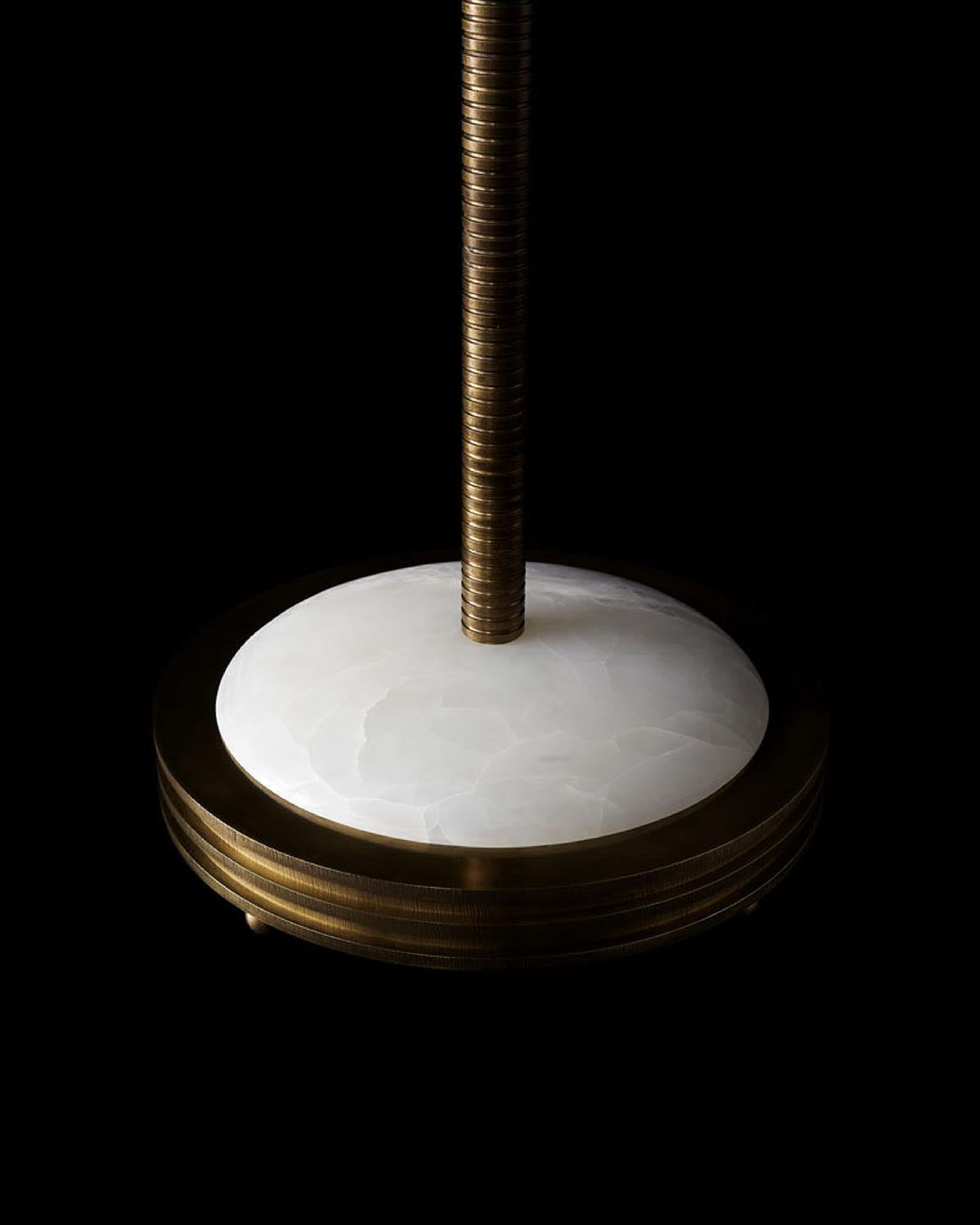 Close-up of hand-embroidered floor lamp base with white textured stone and brass cylindrical rod on black background