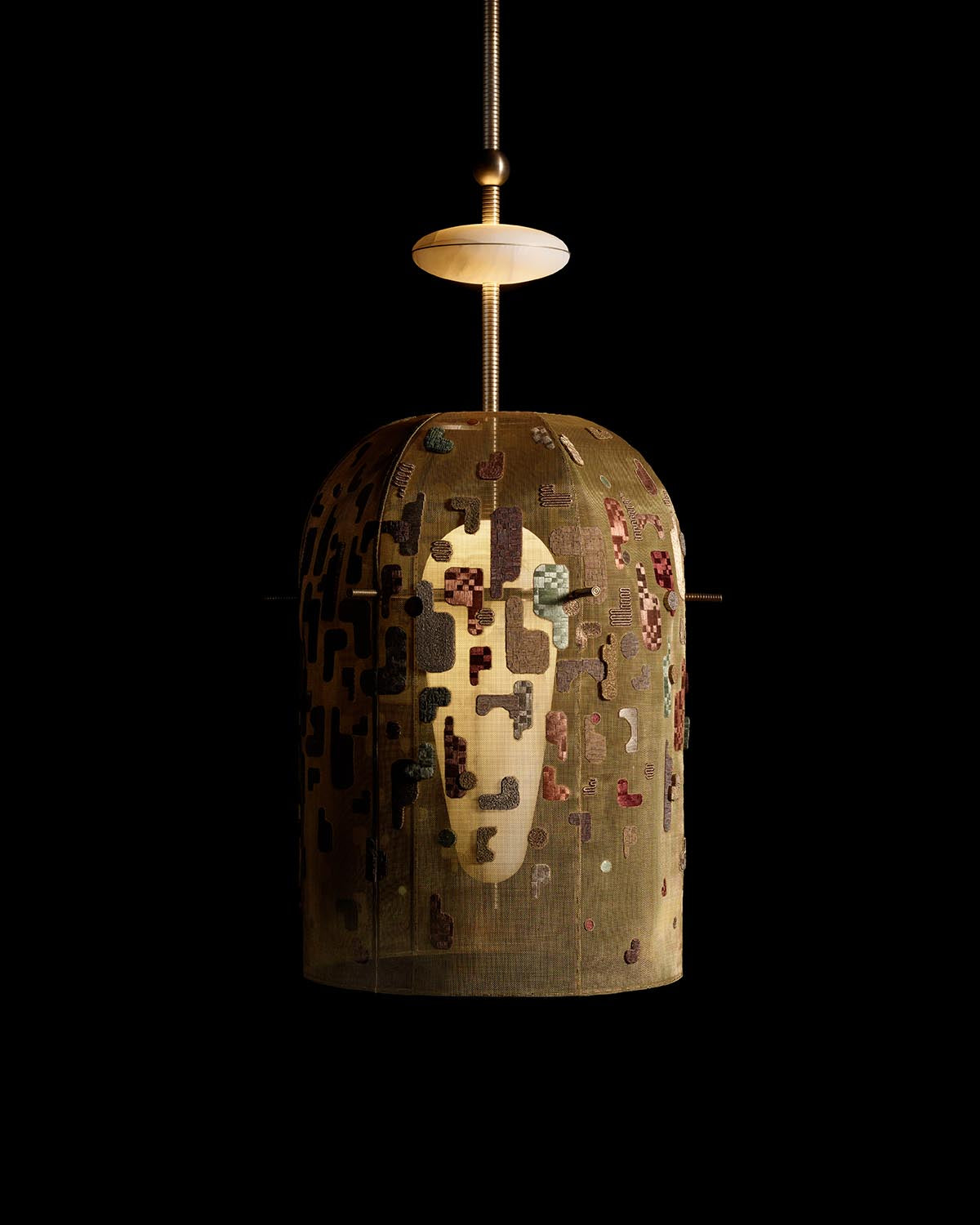 Close-up of hand-embroidered hanging lamp with abstract geometric patterns and muted earthy tones on black background