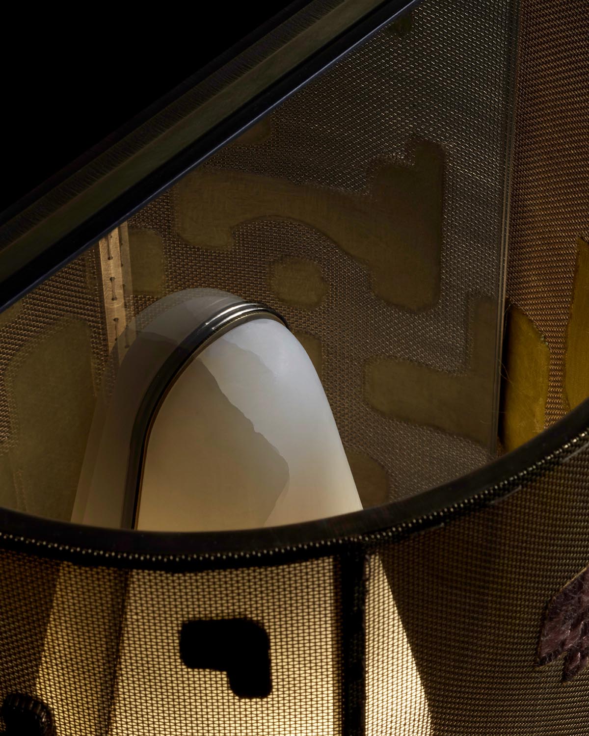 Close-up of a softly glowing hand-embroidered fabric sconce with layered textile and mesh details in warm tones