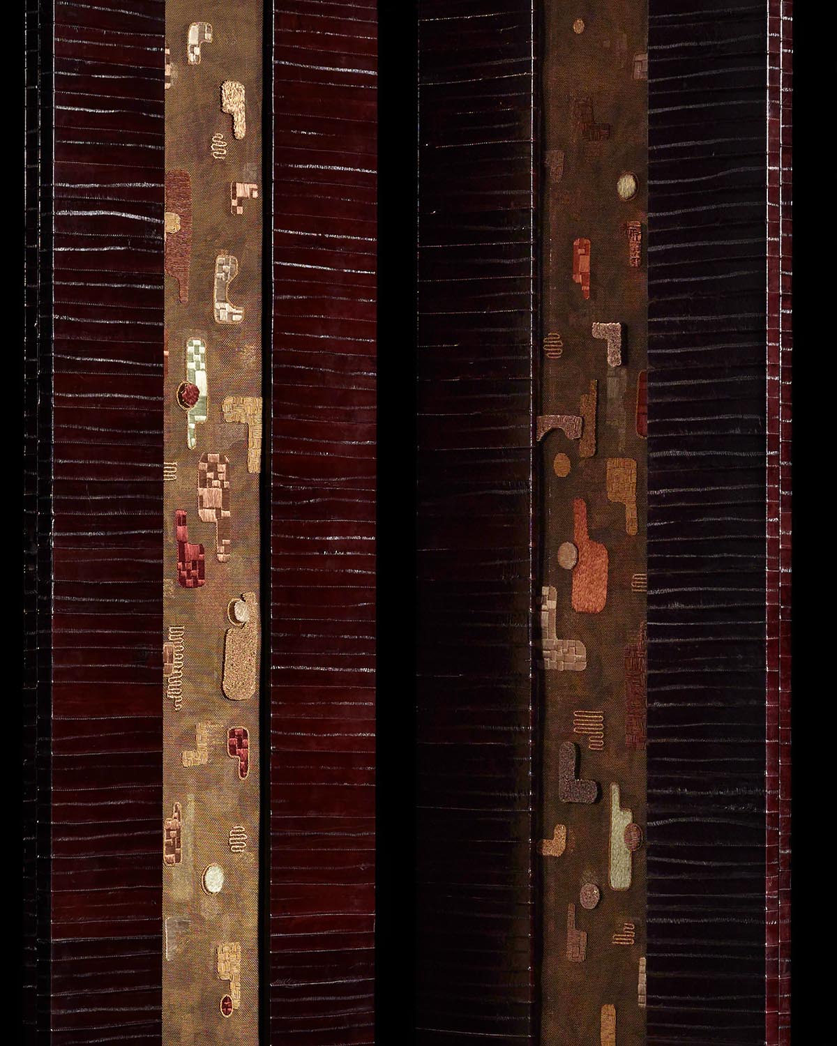 Close-up of two vertical hand-embroidered fabric panels with abstract geometric patterns on deep burgundy and brown backgrounds
