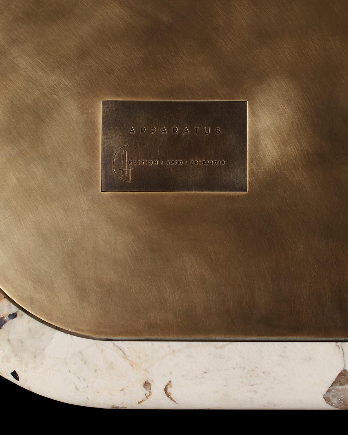 Close-up of a brass plaque with embossed APPARATUS text on a bronze surface above a white marble base