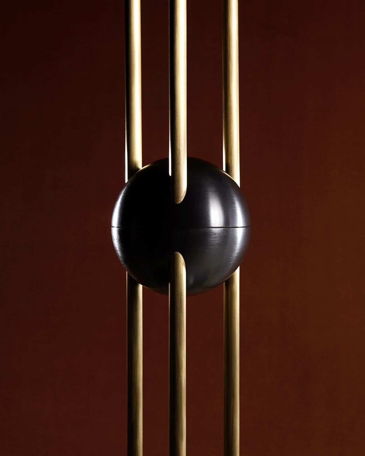 Close-up of a black spherical pendant light suspended among vertical brass rods against a dark brown background
