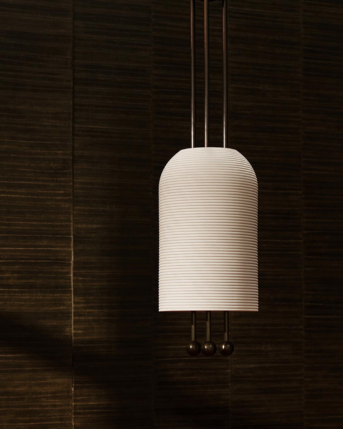 Vertical white ribbed pendant lantern suspended by three thin metal rods against a dark textured background