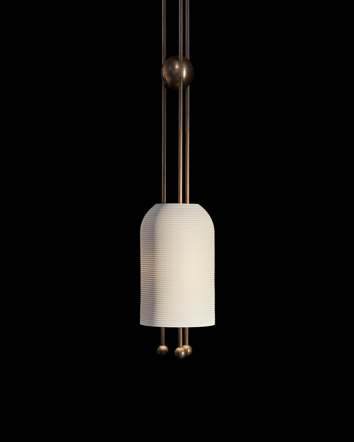 Pendant light fixture with a ribbed white cylindrical shade suspended by three slender brass rods on black background