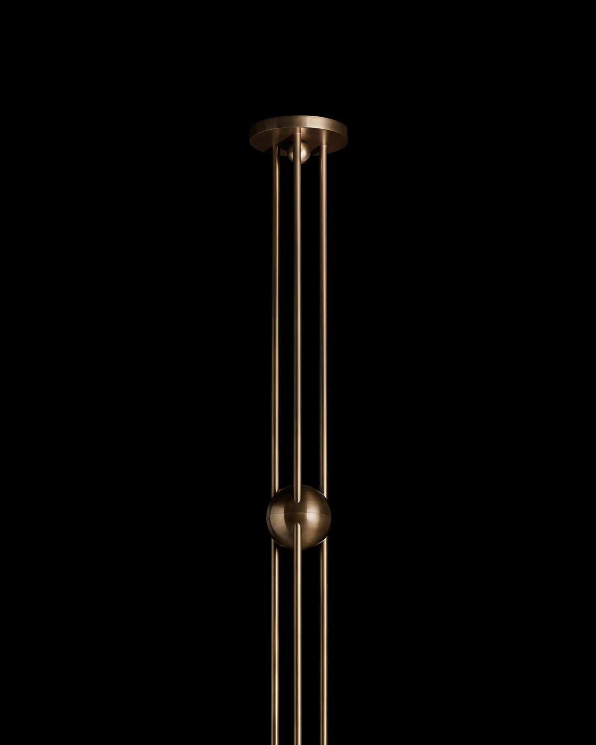 Brushed brass ceiling fixture with three vertical rods connected by a central spherical joint against black background