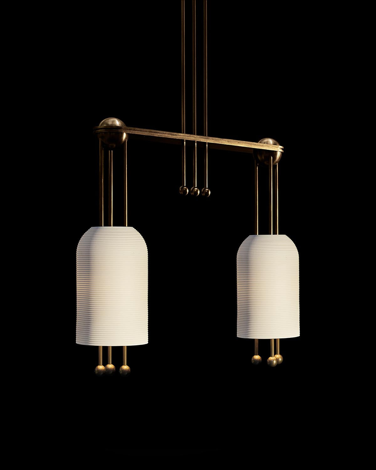 Two pendant lanterns with ribbed white glass shades and brass metal frame against a black background