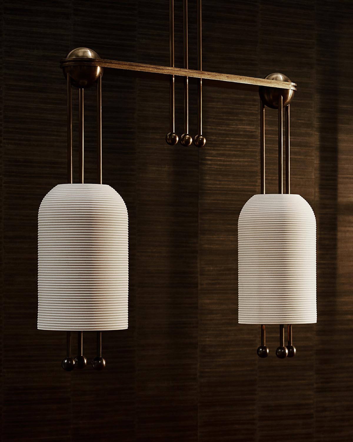 Two white ribbed cylindrical pendant lanterns hanging from a dark bronze horizontal bar against a textured dark background