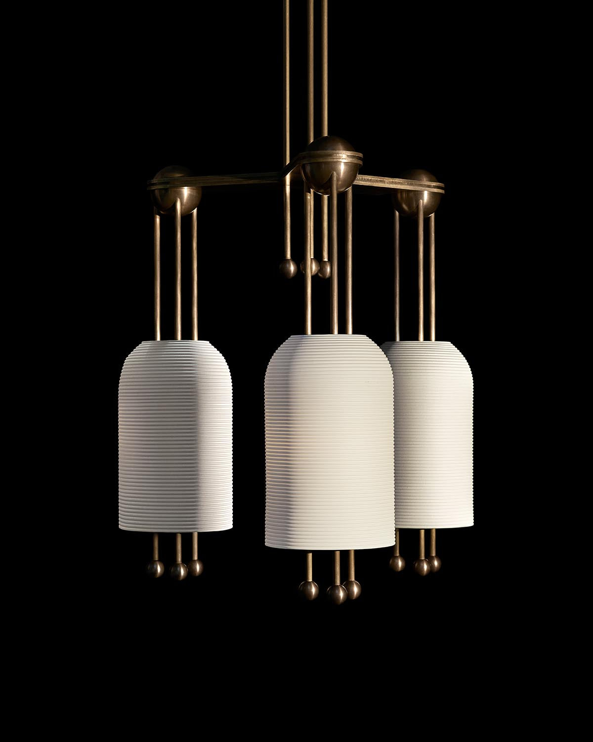 Three white ribbed cylindrical pendant lights with bronze metal fixtures suspended against black background